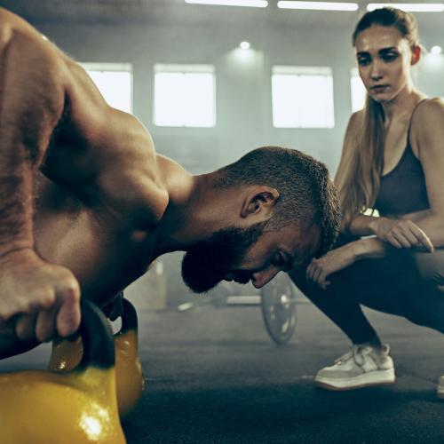 Trener w studio fitness obok klienta wykonującego ćwiczenia, zapewniając indywidualne wsparcie podczas treningu.