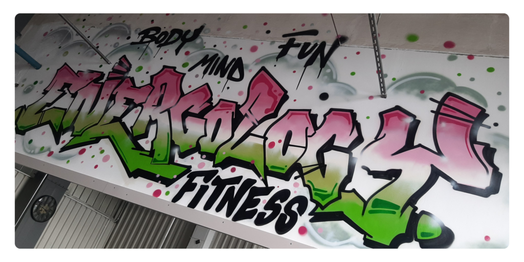 Graffiti z logo studio fitness Energologyfitness na ścianie studia, symbolizujące energię, równowagę ciała i umysłu oraz zabawę. Podejmij kontakt.